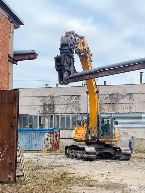 Kollane ekskavaator teisaldab metallkonstruktsiooni tehasehoone ees